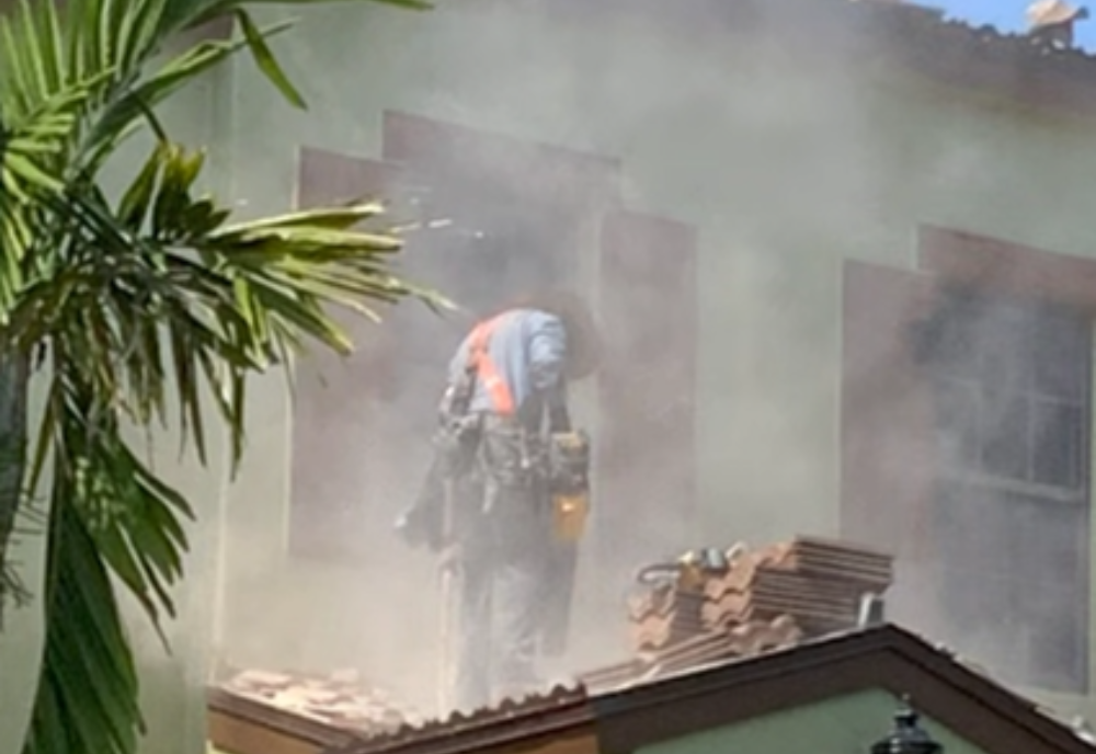 A worker is cutting roof tiles under a cloud of dust.