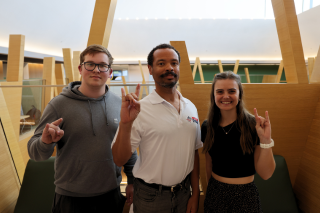 Honors students Tyler Briggs, Mykyta Nechaiev, and Dr. Michael Cross pose while making Go Bulls signs in the bright Judy Genshaft Honors College atrium