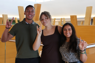 Judy Genshaft Honors College students Breno Nery Dantas, Jamie Powers, and Reva Gandhi pose while making "Go Bulls" hand signs inside of the Honors College building.