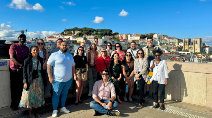 A large group of USF faculty pose in front of the Lisbon Skyline