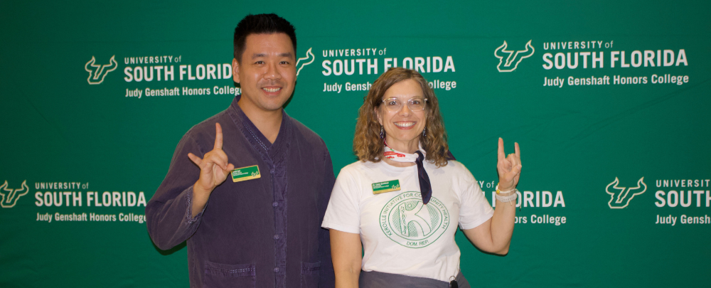 Program leads, Kevin Lee and Dr. Lindy Davidson smile infront of a USF themed backdrop. 