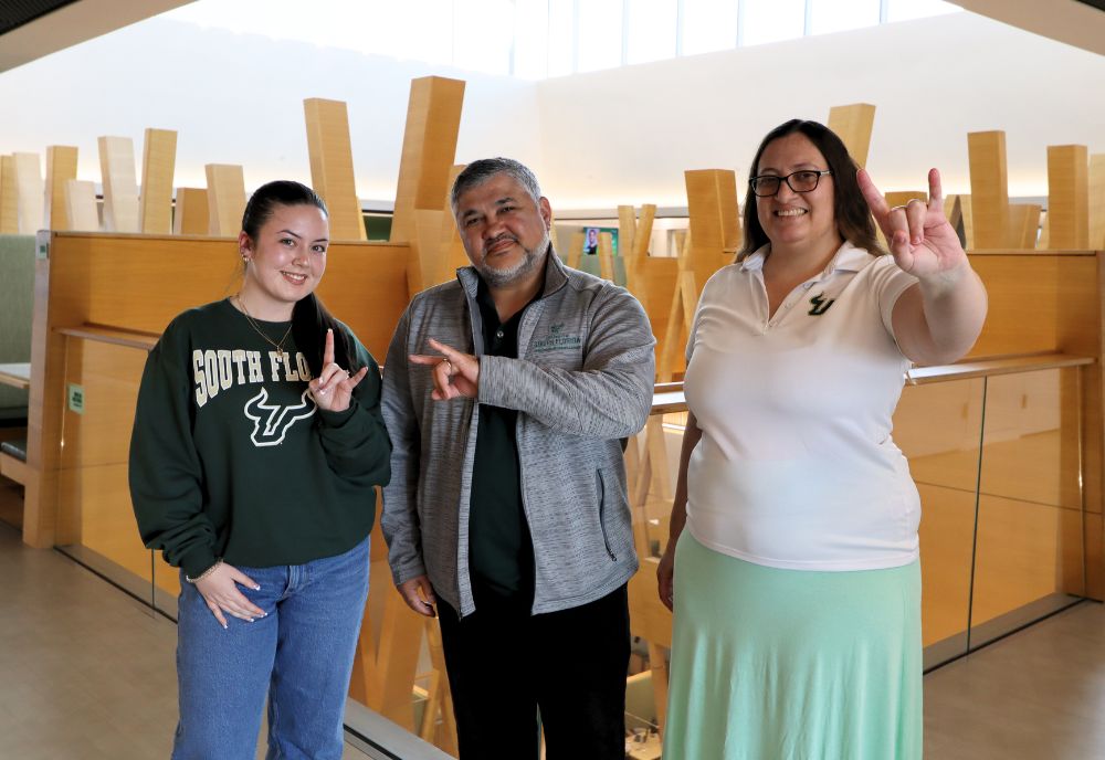 From Left to Right: Ava Gomez, Arnaldo Mejias, and Krysta Banke hold up the go Bulls sign in the Honors atrium