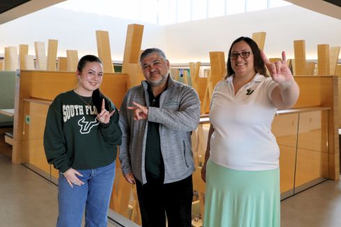 From Left to Right: Ava Gomez, Arnaldo Mejias, and Krysta Banke hold up the go Bulls sign in the Honors atrium