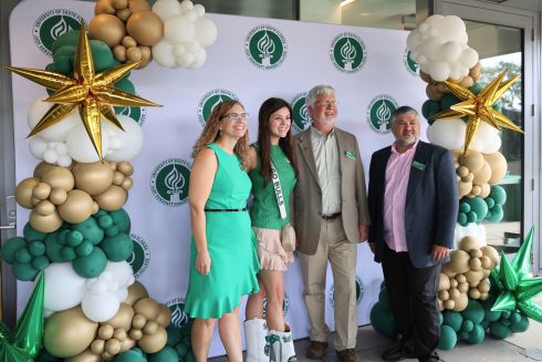 Lindy Davidson, Honors alum Avalon Jade Theisen, Dean Adams, and advisor Arnaldo Mejias pose in front of a backdrop on the patio