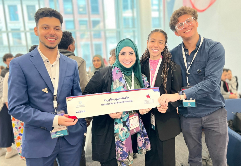 Taha Ahmed Feddoul, professor Raja Benchekroun, Amber Johnson, and Ghali Omar Boutaib smile while holding the USF banner at the competition