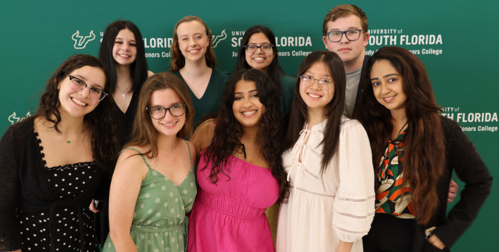 Nine student leaders from the Judy Genshaft Honors College student council executive board pose in front of a green step and repeat