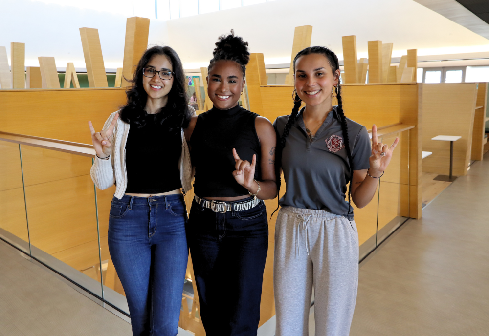 Serena Bhaskar, Karla Evangelista De La Rosa, and Arelis Rodriguez Martinez make Go Bulls signs while posing in the Judy Genshaft Honors College