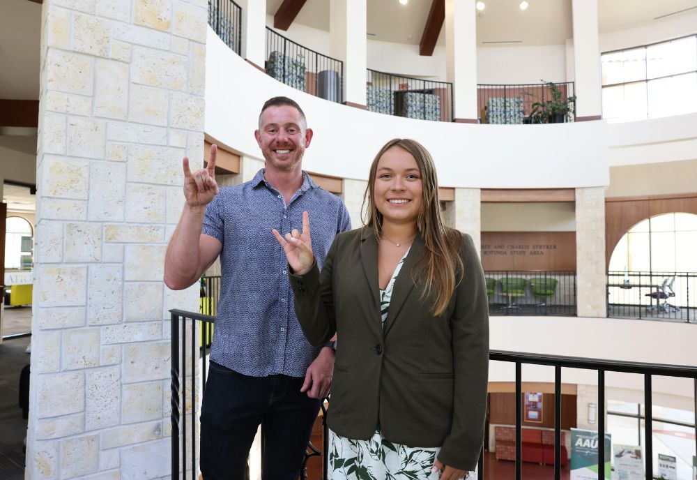 Professor Jordan Howell and Kaylee Eckelman pose with the "Go Bulls" sign in the Sarasota campus atrium.