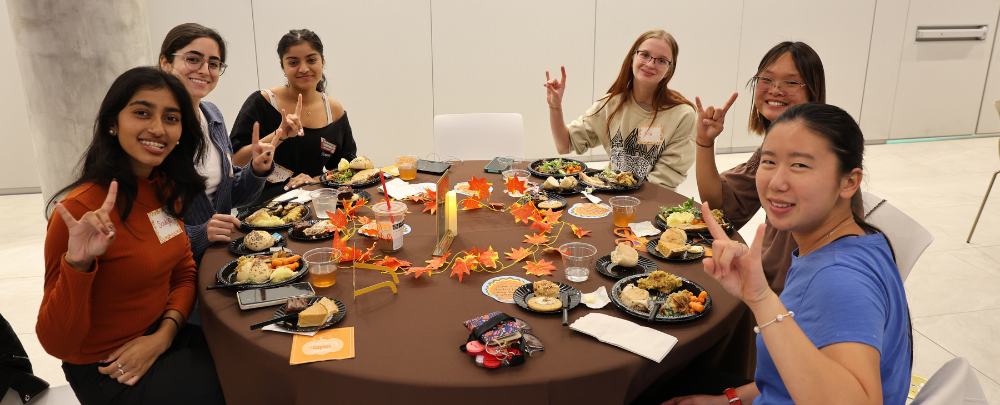 Honors students sit around a table and smile with their Thanksgiving dinners.