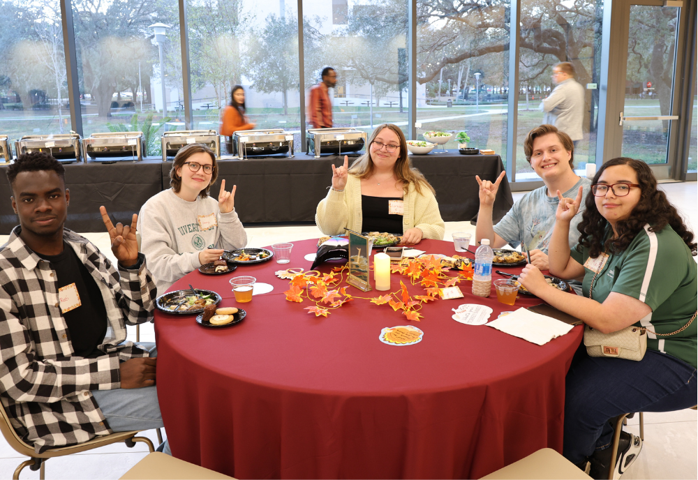 Students smile around a table at the Judy Genshaft Honors College Friendsgiving event.