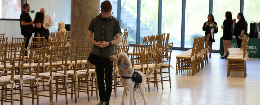 Honors student smiles with his service dog at the graduation celevbration