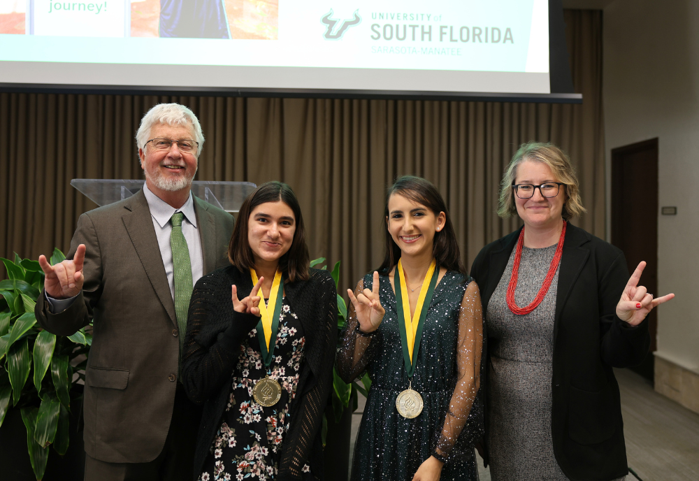 Judy Genshaft Honors College Dean Charles Adams and Assistant Dean Cayla Lanier pose with new Honors graduates Saleha Salek and Diana Labrador and the 2024 Honors Symposium in the Sarasota-Manatee campus's Selby Auditorium.