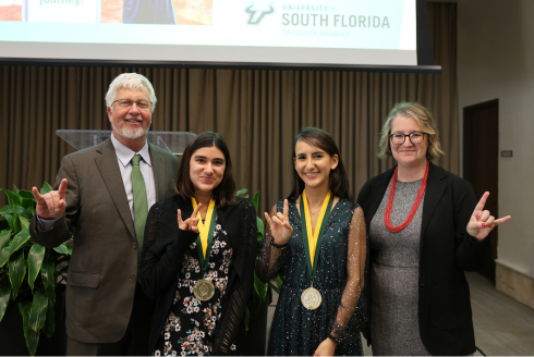 Judy Genshaft Honors College Dean Charles Adams and Assistant Dean Cayla Lanier pose with new Honors graduates Saleha Salek and Diana Labrador and the 2024 Honors Symposium in the Sarasota-Manatee campus's Selby Auditorium.