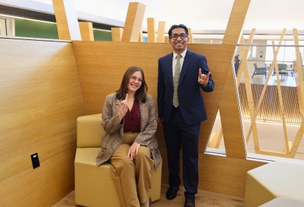 Claire Kooy (seated) and Alvin Varghese (standing) pose with the "Go Bulls" hand sign in the Honors building