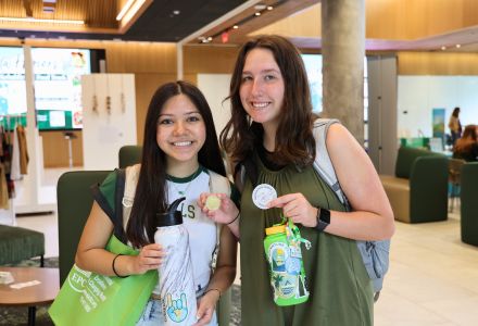 Two participants of the 2024 Climate Teach-In posing in the Honors atrium with stickers and hand-outs from the event.