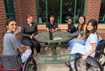 Students in Romano's class sit around a picnic table with two using mobility equipment