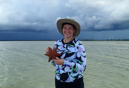 USF St. Petersburg Honors alum Gabby Schwager poses with a starfish in front of the water on Andros Island in the Bahamas.