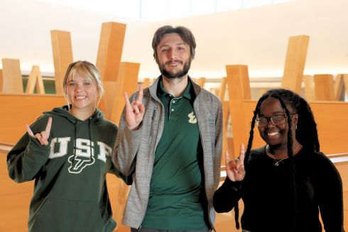 Nora Wolfgang, Marco Nardiello, and Whitney Louis pose for a photo on the fifth floor of the Honors building, holding up the 