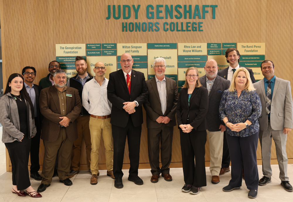 Judy Genshaft Honors College leadership and Veterans Affairs Health Care representatives pose as a group in the Zimmerman Family Foundation Atrium in front of a recognition wall.