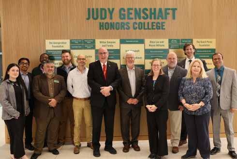 Judy Genshaft Honors College leadership and Veterans Affairs Health Care representatives pose as a group in the Zimmerman Family Foundation Atrium in front of a recognition wall.