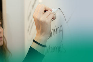 womans hand up close writing on whiteboard