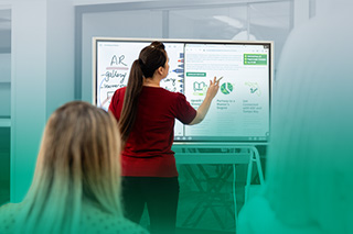 A woman stands in front of a somone using a smart board