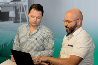 2 men sit on a couch looking at an ipad