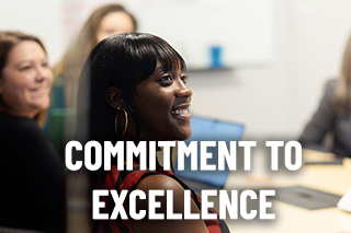 a woman sits at table smiling during a meeting with the words commitment to excellence on top of image