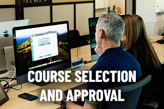 a learning designer sits with a faculty member pointing to a computer screen