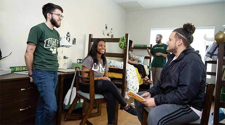 4 students sit and talk inside their dorm room