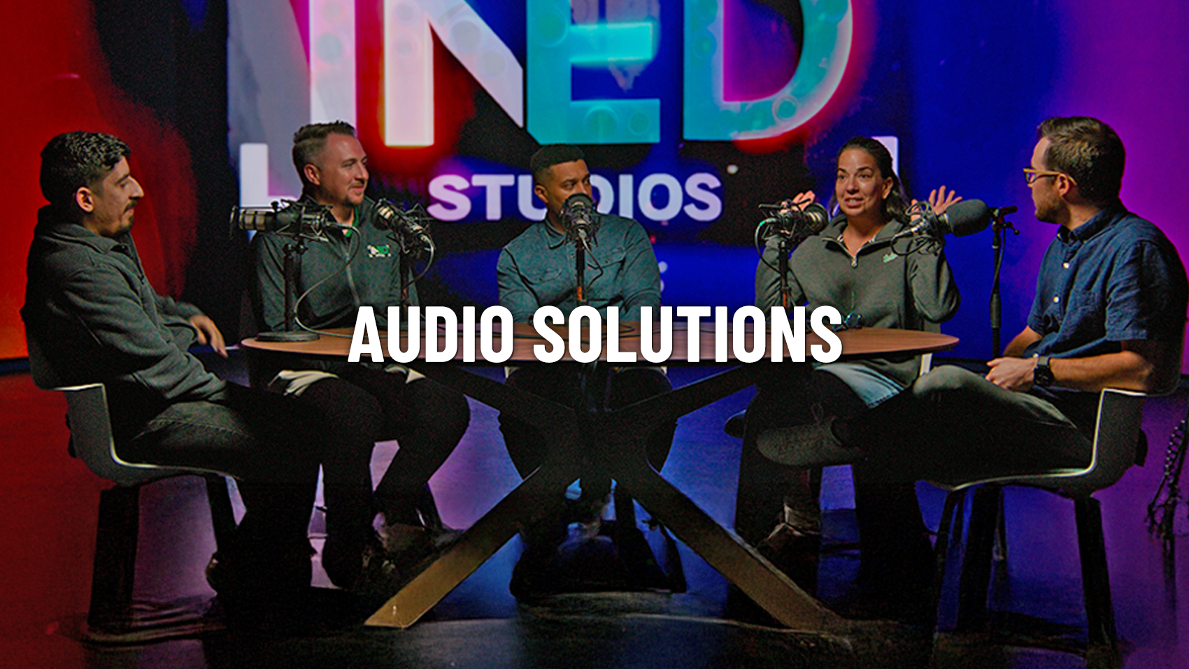 a group of ined studios employees sit around with microphones talking in a podcast