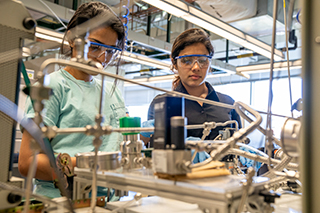 Graduate students Sreya Seby (left) and Umadevi Gopalakrishnan work at a bench scale process setup designed to convert methan/CO2 gas into liquid fuel.