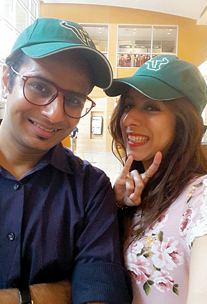Ojas Rawal, a young man of Indian descent, poses with his sister, Khushali. The two are wearing green USF caps adorned with the iconic Bull U symbol, and she makes the USF ‘horns-up’ hand symbol.