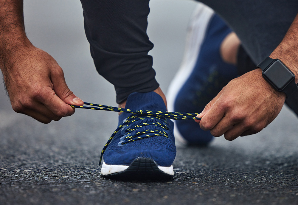 a person tying their running shoes with an Apple Watch on