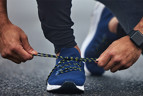 a person tying their running shoes with an Apple Watch on