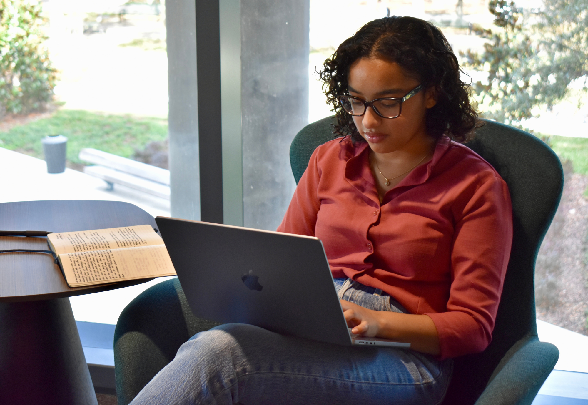  USF student Avani Sanghvi sits in a modern-design chair, focused on a laptop resting on her lap.