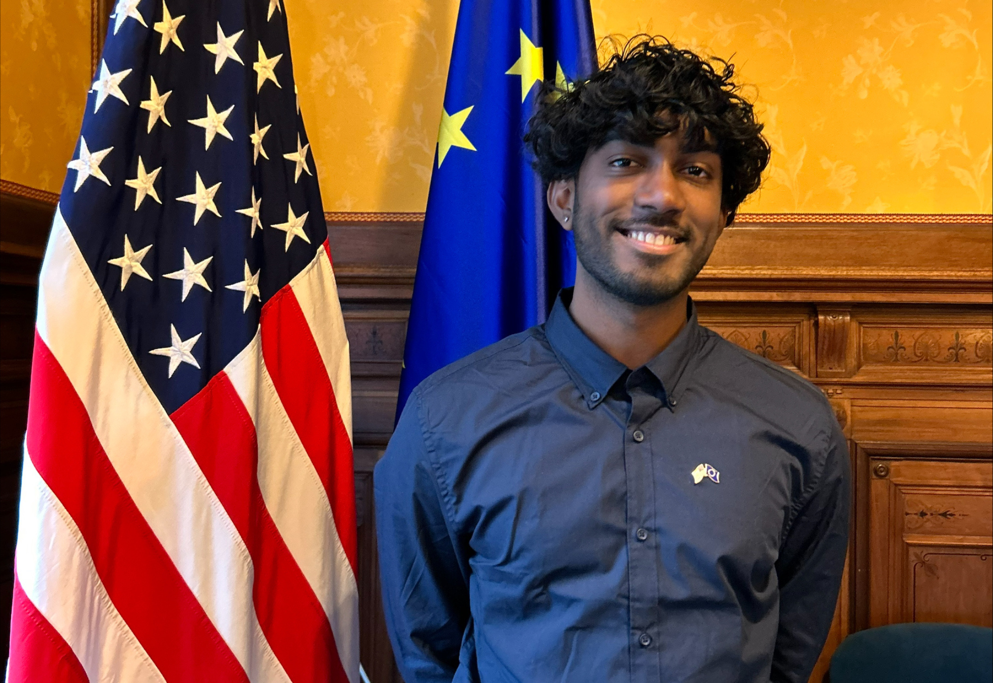 Kavi Ackloo standing in front of American and European Union flags