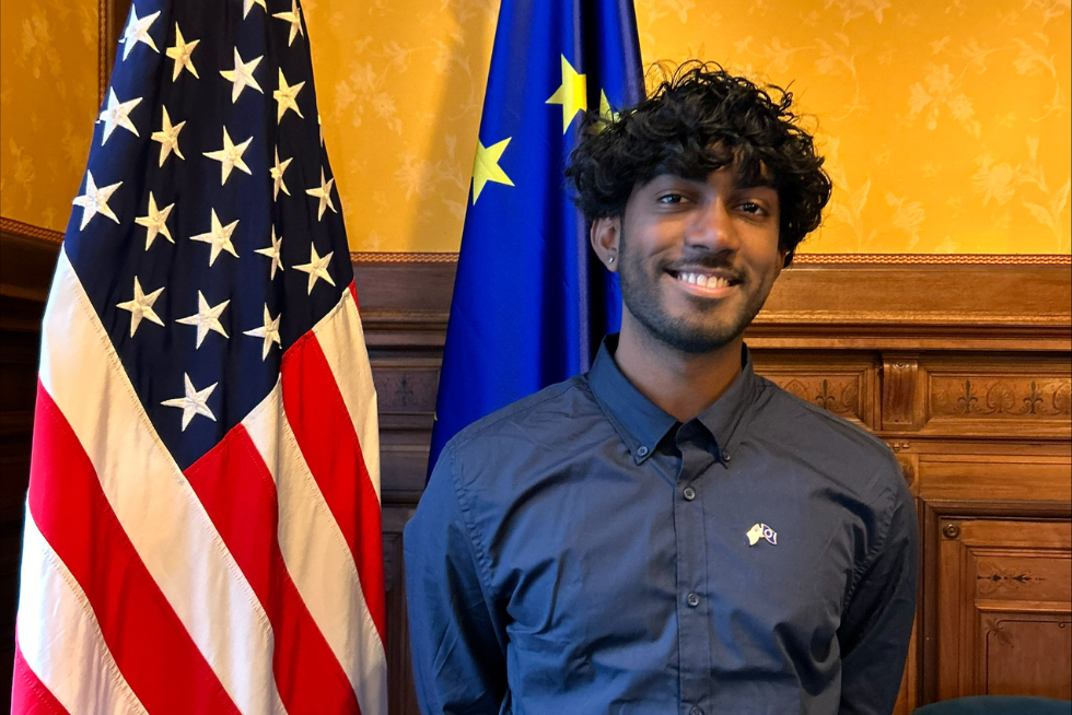 Kavi Ackloo standing in front of American and European Union flags