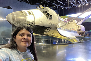 Student Andrea Coloma in front of a space shuttle on display at NASA