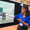 female in blue shirt with dark hair presents her research poster at the Undergraduate Research Conference