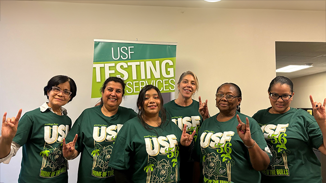 a group of testing services employees pose with their horns up hand sign. 