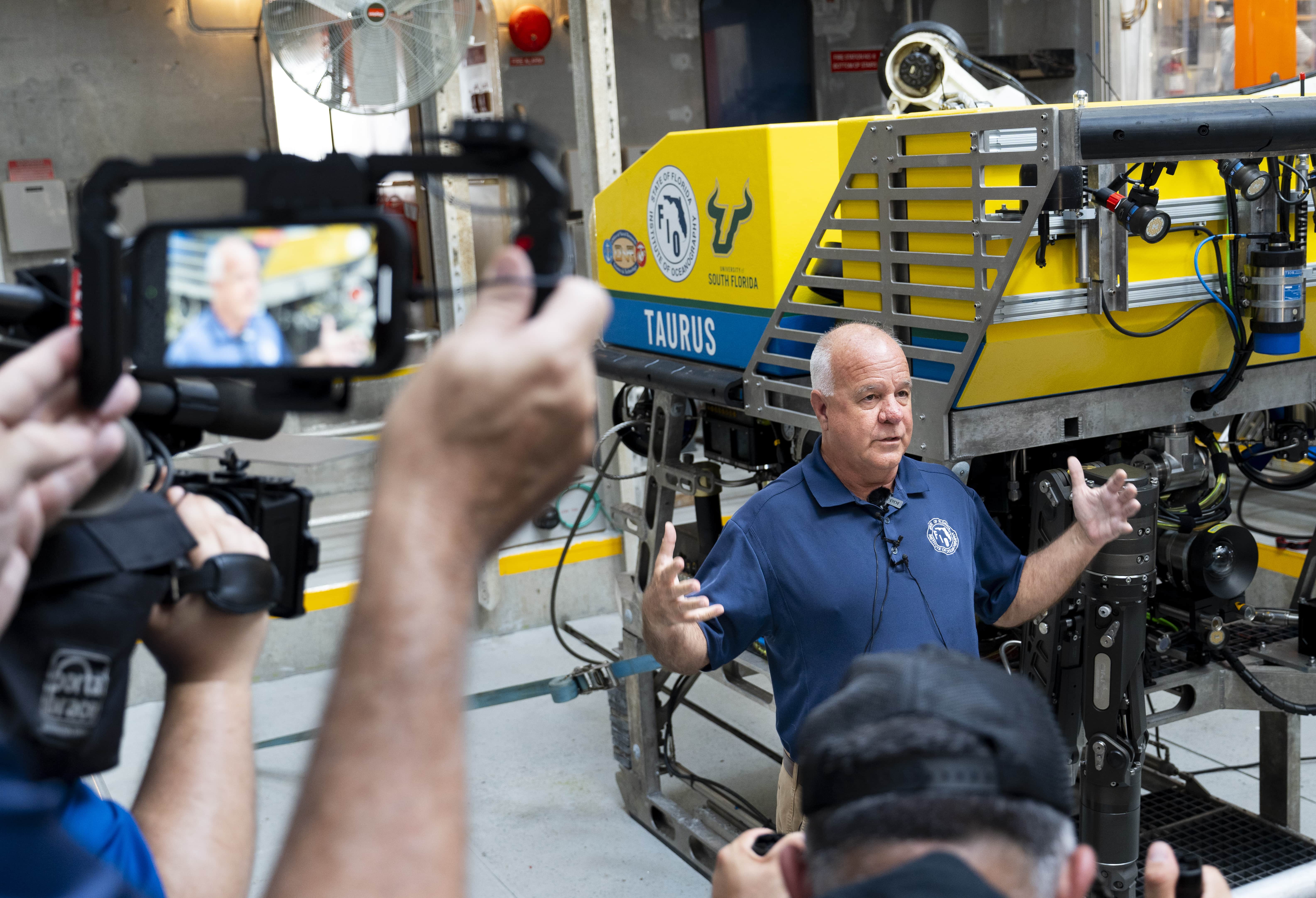 Person filming a man describing the functionality of the The ROV Tauru, a sophisticated, remotely operated vehicle that can reach ocean depths of up to 2.5 miles.