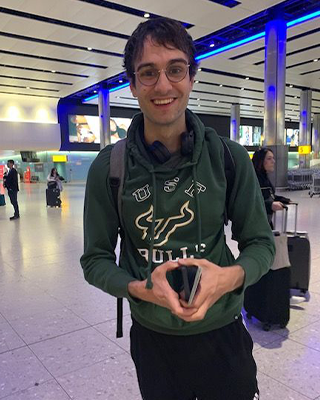 Oxford Postdoctoral researcher James Anibal smiles at the camera in the aiport in a green and white USF sweatshirt