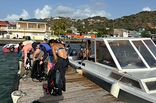 USF students prepare on a dock to scuba dive. A boat is beside them