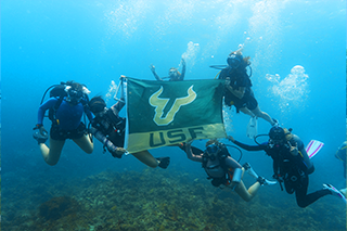 USF students under the sea in scuba diving gear and holding the USF banner