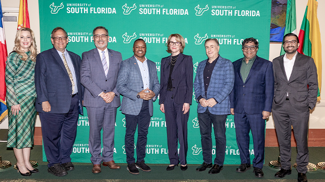 Panelists and speakers smiling in front of country flags and USF green backdrop