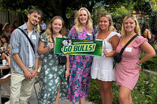 Dr. Kiki posing with alumni and holding a green banner that reads "Go Bulls"