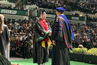 Vietnamese student, Kha So dressed in graduation regalia and shaking the hand at commencement of an administrator on the stage