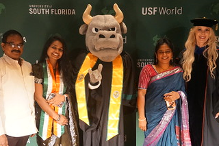 Vice President of USF World, Dr. Kiki Caruson, stands with the school's bull mascot, ROcky, two Indian international students, and their parents following the 2024 Spring sash ceremony