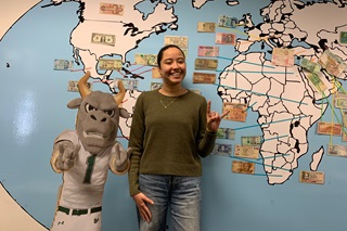 female Colomb ian student at USF posing in front a map of the world with international currencies taped by their respective countries